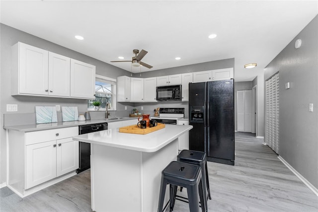 kitchen featuring white cabinets, a breakfast bar, light wood-type flooring, black appliances, and a center island