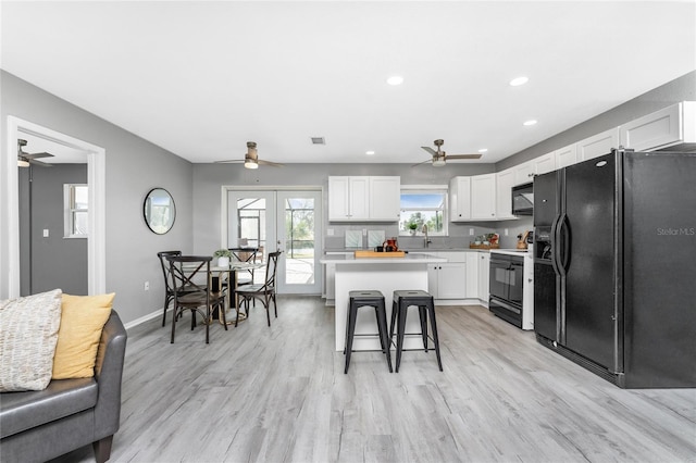 kitchen featuring light hardwood / wood-style floors, white cabinets, black appliances, and a kitchen bar