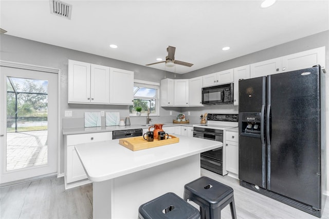 kitchen featuring black appliances, white cabinets, a kitchen bar, and a kitchen island