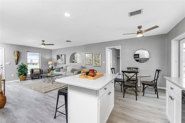 kitchen with a kitchen island, light hardwood / wood-style flooring, a breakfast bar, white cabinets, and ceiling fan