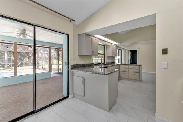 kitchen featuring dark stone counters, a healthy amount of sunlight, vaulted ceiling, and kitchen peninsula