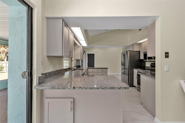 kitchen featuring appliances with stainless steel finishes, kitchen peninsula, sink, and stone counters