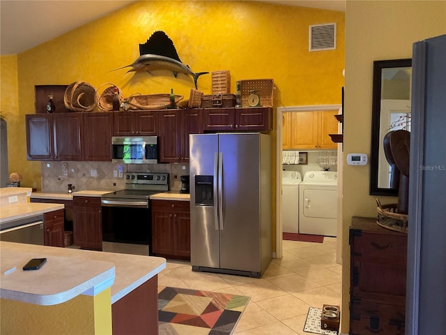 kitchen with backsplash, vaulted ceiling, light tile patterned floors, appliances with stainless steel finishes, and washer and dryer