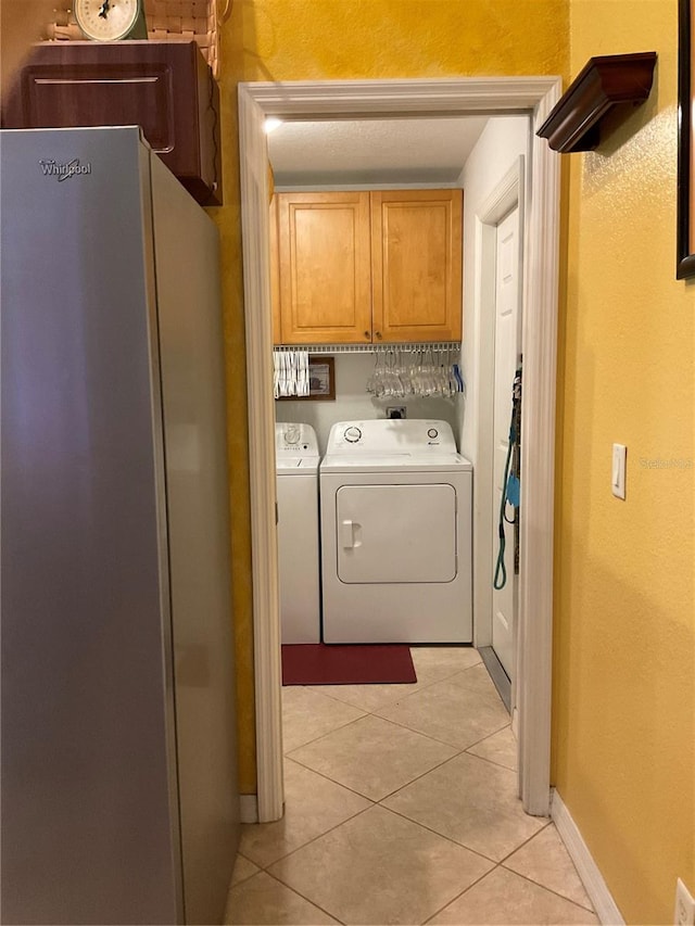 clothes washing area with cabinets, washing machine and clothes dryer, and light tile patterned floors