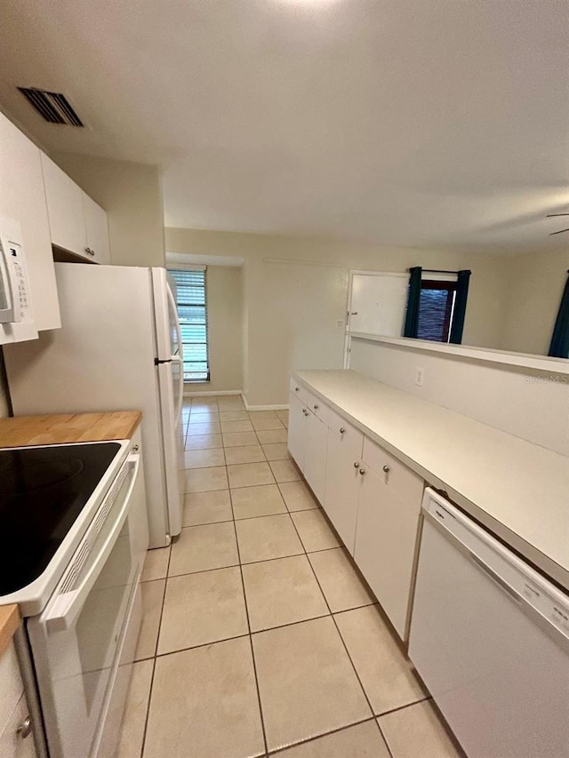 kitchen featuring white appliances, light tile patterned flooring, and white cabinets