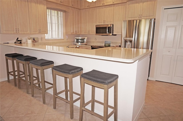 kitchen with appliances with stainless steel finishes, kitchen peninsula, a kitchen bar, and light tile patterned floors