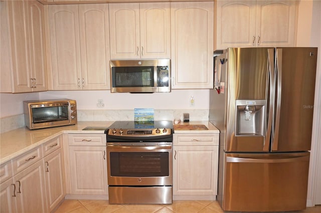 kitchen with appliances with stainless steel finishes, light tile patterned flooring, and light brown cabinetry