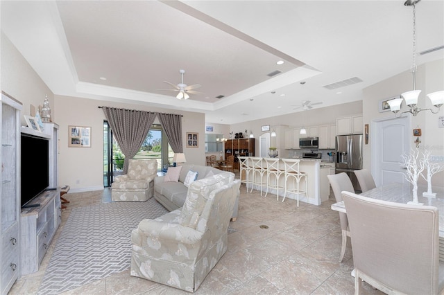 living room featuring a tray ceiling and ceiling fan with notable chandelier