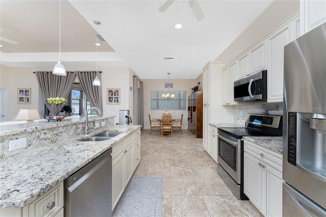 kitchen with light stone countertops, appliances with stainless steel finishes, sink, and hanging light fixtures