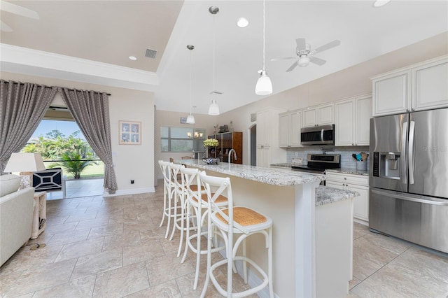 kitchen featuring light stone countertops, appliances with stainless steel finishes, a kitchen island with sink, and white cabinetry