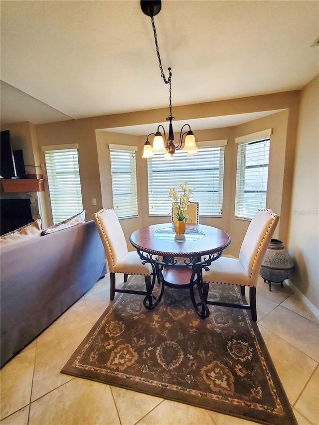 dining space featuring a chandelier, light tile patterned flooring, a stone fireplace, and a healthy amount of sunlight