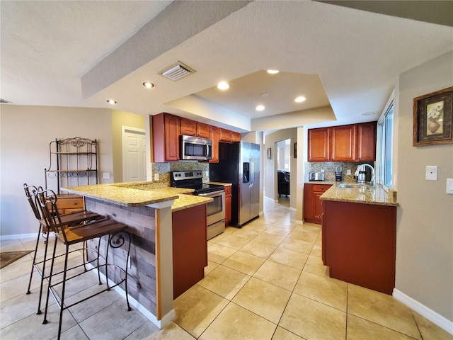 kitchen featuring decorative backsplash, a kitchen breakfast bar, kitchen peninsula, stainless steel appliances, and a tray ceiling