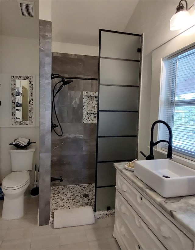 bathroom featuring vanity, a tile shower, toilet, and tile patterned floors