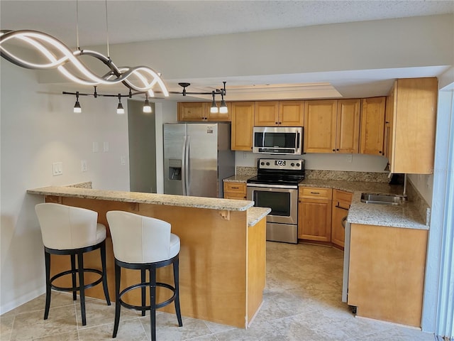 kitchen featuring a kitchen bar, kitchen peninsula, sink, pendant lighting, and appliances with stainless steel finishes