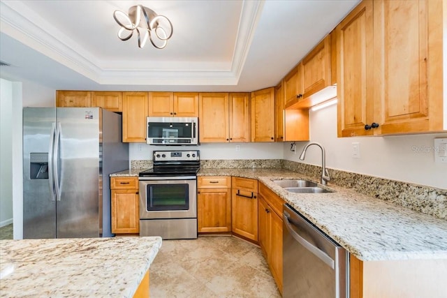 kitchen featuring sink, ornamental molding, a tray ceiling, light stone countertops, and appliances with stainless steel finishes