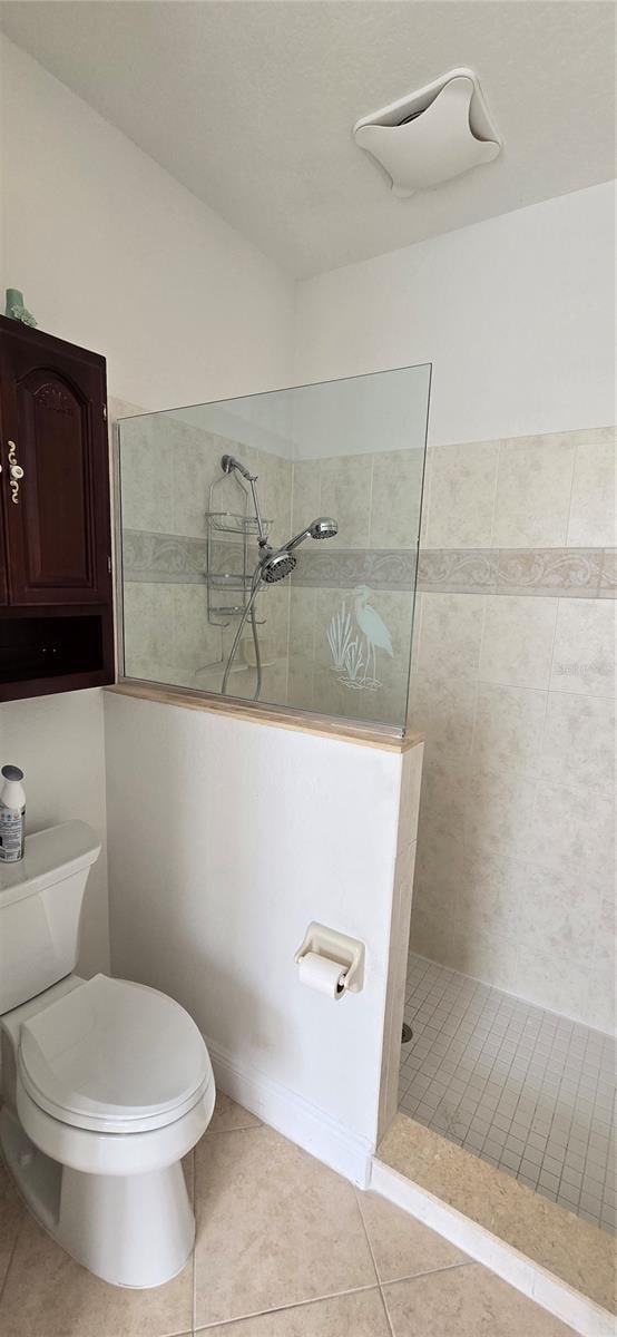 bathroom with toilet, tile patterned flooring, and tiled shower