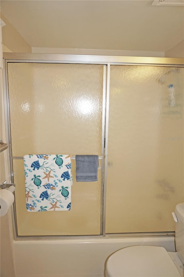 bathroom featuring bath / shower combo with glass door and toilet