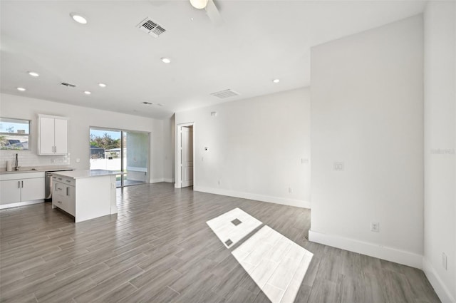 interior space with light hardwood / wood-style flooring, white cabinets, sink, and a kitchen island