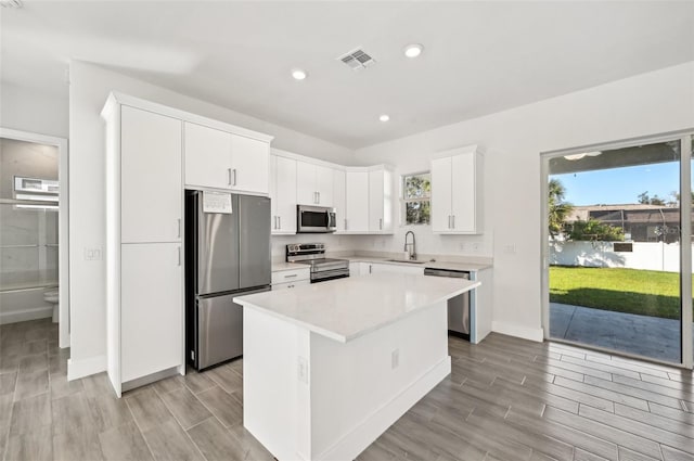 kitchen with a kitchen island, light hardwood / wood-style flooring, sink, white cabinetry, and appliances with stainless steel finishes