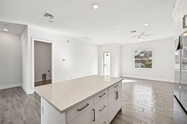 kitchen featuring ceiling fan, white cabinetry, light stone countertops, light hardwood / wood-style flooring, and a center island