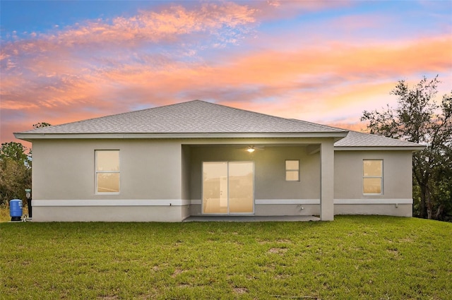 back house at dusk featuring a patio and a lawn