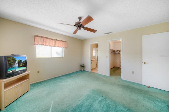 unfurnished bedroom with a closet, light carpet, a spacious closet, a textured ceiling, and ceiling fan