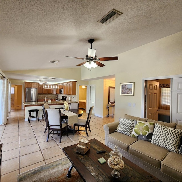 living room featuring lofted ceiling, a textured ceiling, light tile patterned floors, and ceiling fan