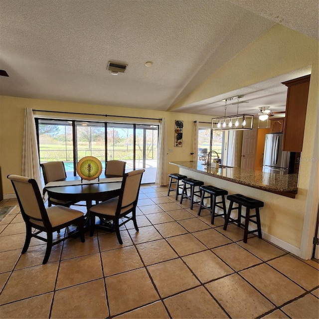 dining area featuring a textured ceiling, ceiling fan, light tile patterned floors, and vaulted ceiling