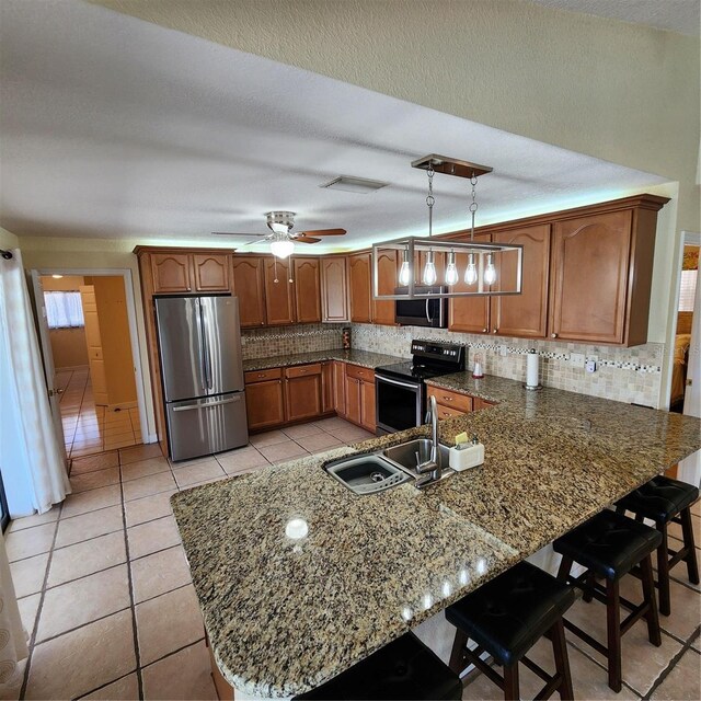 kitchen featuring kitchen peninsula, light tile patterned floors, appliances with stainless steel finishes, a kitchen breakfast bar, and pendant lighting