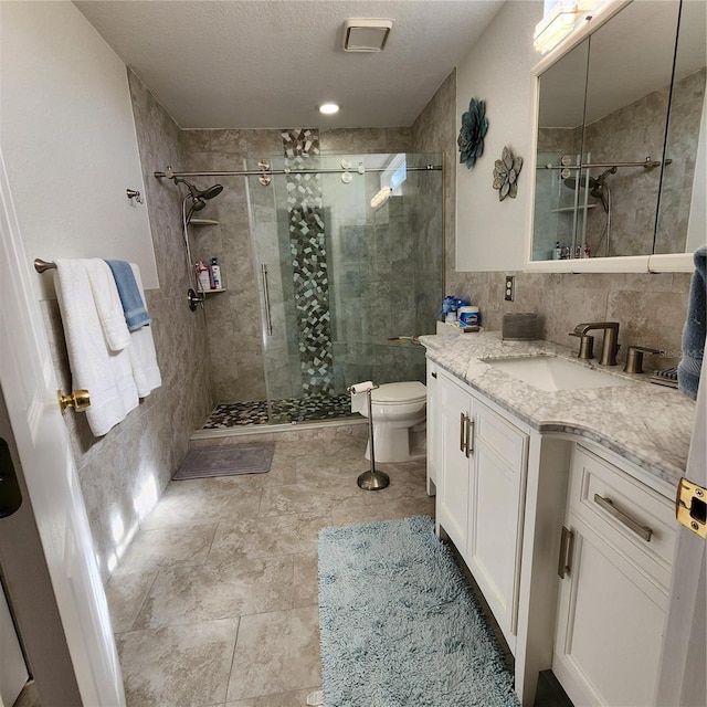 bathroom featuring a textured ceiling, toilet, walk in shower, tile walls, and vanity