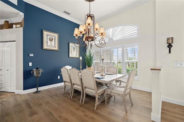 dining area with wood-type flooring, ornamental molding, and an inviting chandelier