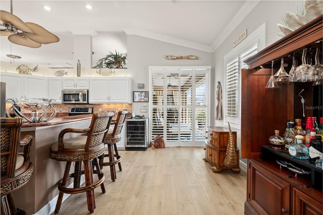 kitchen featuring backsplash, wine cooler, vaulted ceiling, crown molding, and white cabinets