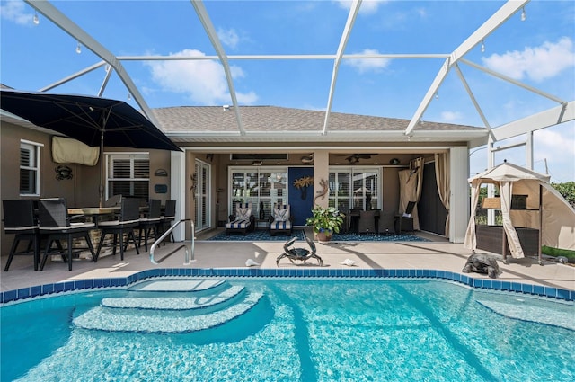 view of swimming pool featuring ceiling fan, glass enclosure, and a patio