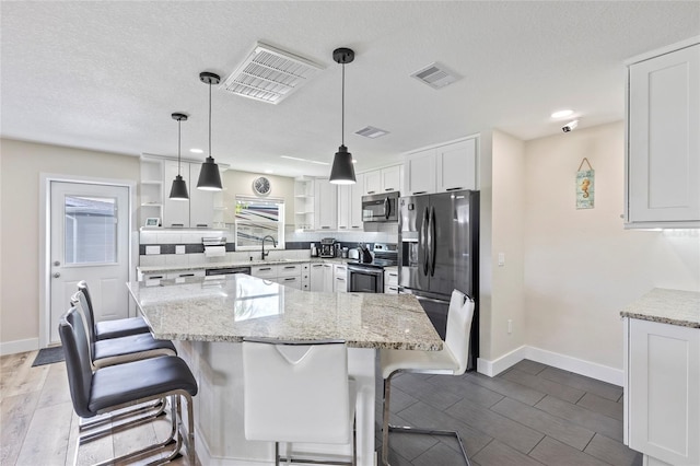 kitchen with sink, white cabinetry, stainless steel appliances, a center island, and decorative light fixtures