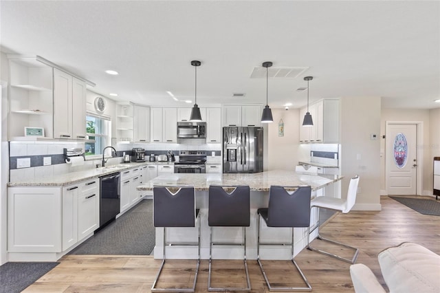 kitchen with white cabinets, a center island, light hardwood / wood-style floors, stainless steel appliances, and light stone countertops