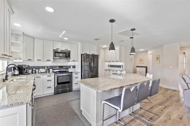 kitchen featuring appliances with stainless steel finishes, decorative light fixtures, white cabinetry, sink, and a center island