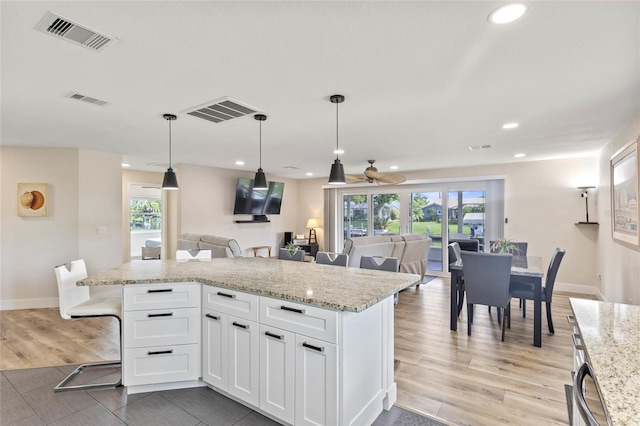 kitchen featuring white cabinetry, light stone countertops, pendant lighting, and light hardwood / wood-style floors