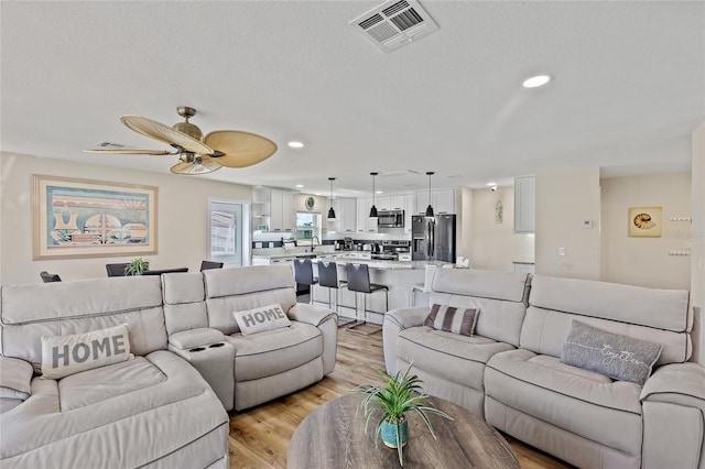 living room featuring sink, a textured ceiling, ceiling fan, and light wood-type flooring