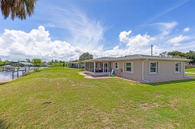 back of house with a water view, a sunroom, and a lawn