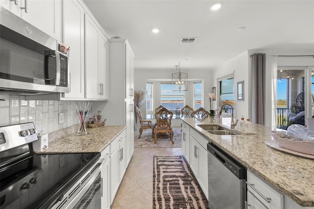 kitchen with sink, stainless steel appliances, white cabinets, a notable chandelier, and decorative backsplash