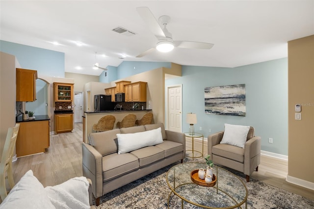 living room featuring light wood-type flooring, vaulted ceiling, ceiling fan, and sink