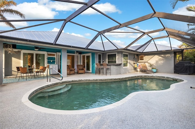 view of pool with a bar, a patio, glass enclosure, and ceiling fan