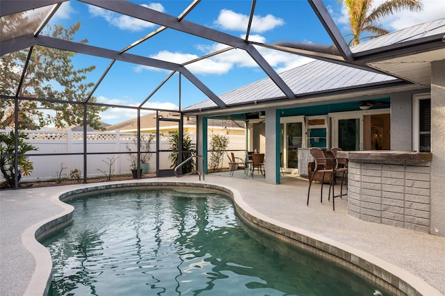 view of swimming pool featuring a patio area, ceiling fan, exterior bar, and glass enclosure