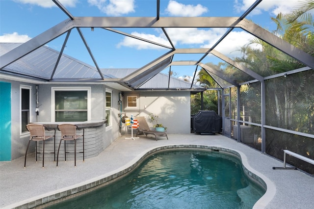 view of pool with exterior bar, glass enclosure, area for grilling, and a patio area