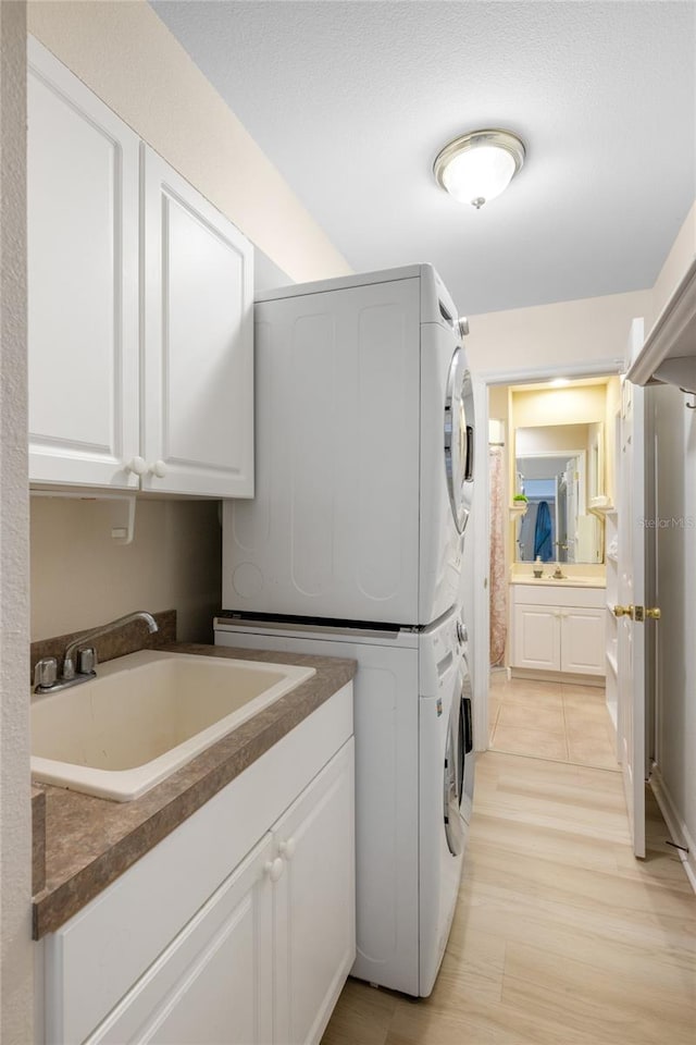 laundry area with cabinets, sink, light wood-type flooring, and stacked washer and dryer