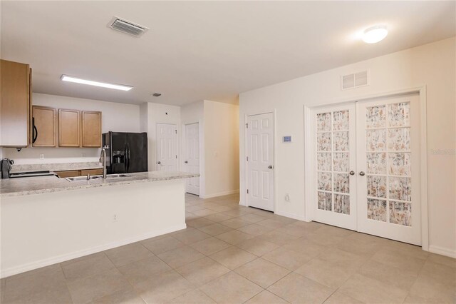 kitchen featuring french doors, black refrigerator with ice dispenser, sink, light tile patterned floors, and range