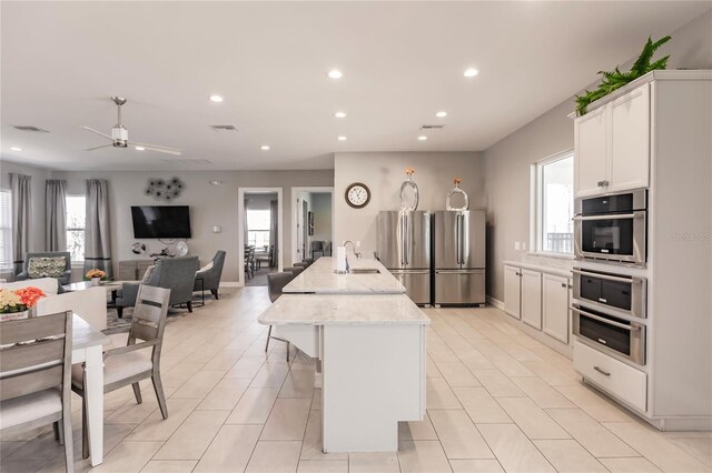 kitchen with an island with sink, stainless steel appliances, sink, light stone countertops, and white cabinetry