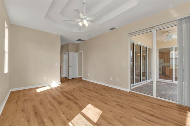 unfurnished room with a raised ceiling, ceiling fan, and light hardwood / wood-style floors