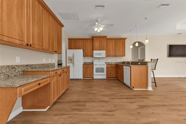 kitchen featuring a breakfast bar, white appliances, hanging light fixtures, light hardwood / wood-style floors, and kitchen peninsula