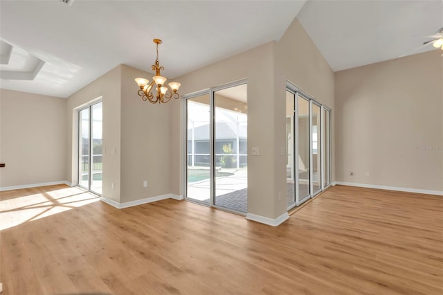 empty room with ceiling fan with notable chandelier, vaulted ceiling, and light hardwood / wood-style flooring